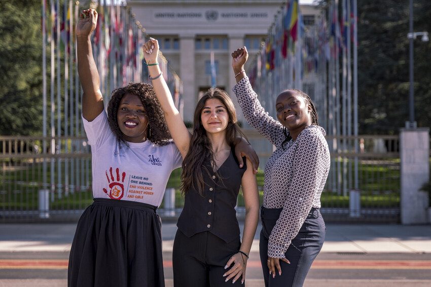 Racheal, Lynne, and Margaret from Plan International's She Leads programme stand outside the Hague with their fists raised up. 